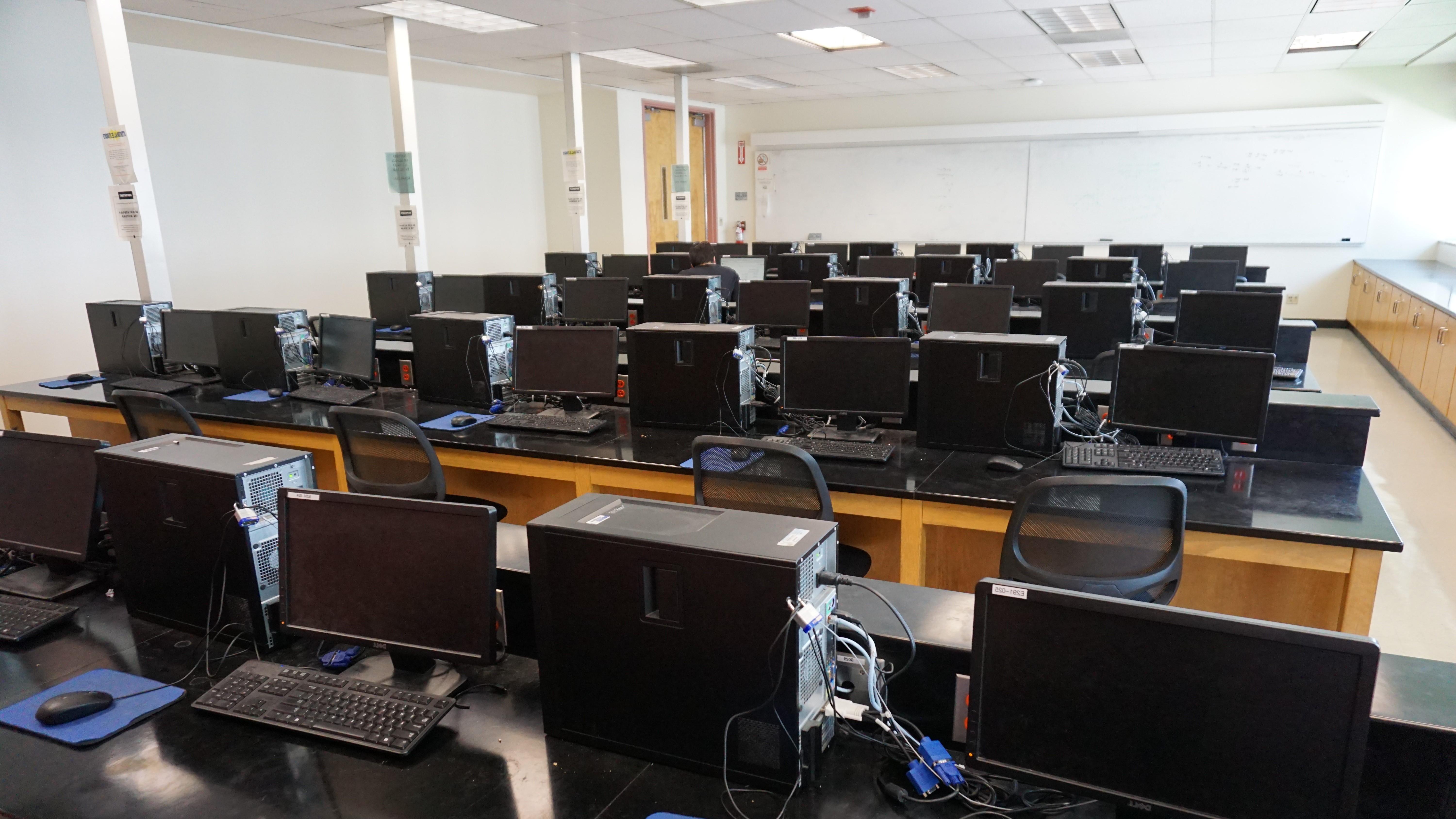 A classroom full of computer stations with whiteboards hanging on every wall.