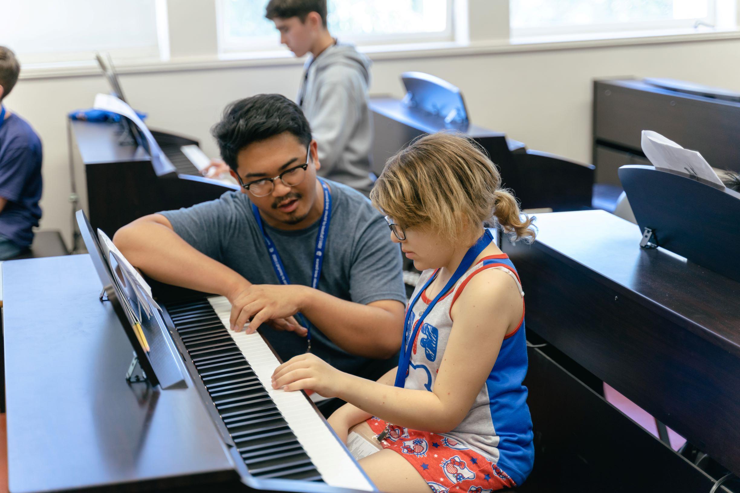 A teacher teaches a young student how to play the keyboard.